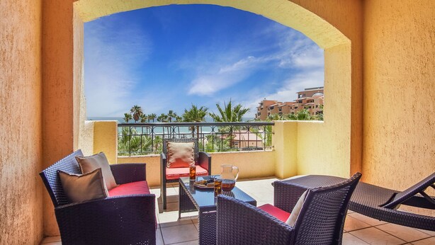 A balcony with wicker furniture, a table, and a view of the ocean and buildings. - Princesa Resort D-307 Pelican's Post Ocean View Chic Condo (Puerto Peñasco)