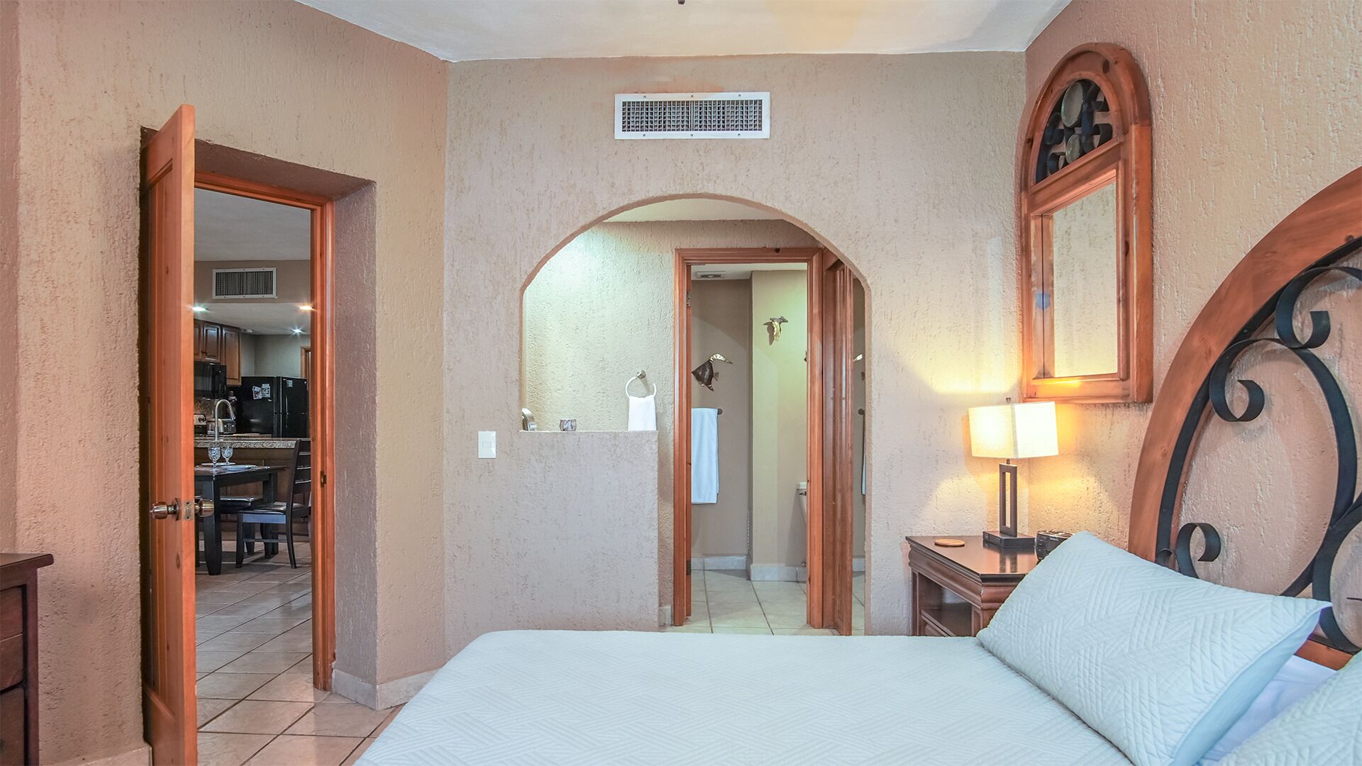 Ein Hotelzimmer mit einem Bett, einem Nachttisch, einer Lampe, einem Rundbogen und Blick zur Küche.
