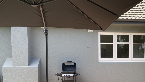 An outdoor patio area with wicker furniture, a barbecue grill, and a ceiling fan. - Twin Cedars Cottage, Havelock North (Havelock North)