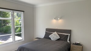 A bedroom with a bed, nightstands, a window, and a wall-mounted light fixture. - Twin Cedars Cottage, Havelock North (Havelock North)