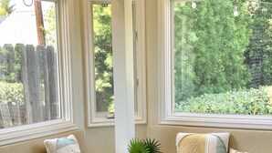 A dining area with a wooden table and patterned chairs, large windows with a view of greenery, and a small potted plant on the table. - Citrus Cottage in Old Town Orange near Chapman U & Disneyland  (Orange)