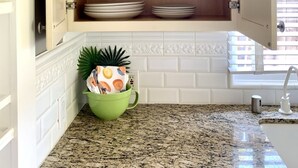 A kitchen with a wooden cabinet containing bowls, plates, and a mug. A green bowl with a plant is on the counter. - Citrus Cottage in Old Town Orange near Chapman U & Disneyland  (Orange)