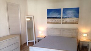 Un dormitorio con cama, mesitas de noche, cómoda y dos cuadros en la pared.