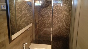 Un baño moderno con cabina de ducha de vidrio, un lavamanos blanco y un espejo grande.