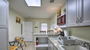 Una cocina con encimera de granito, un fregadero y un microondas. Se ven sillas y una puerta al fondo.
