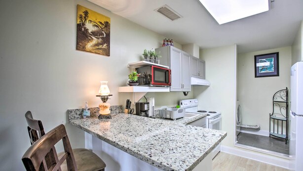 Una cocina con encimera de granito, armarios blancos, microondas y una pequeña isla con asientos.