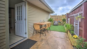 Un patio con mesa y sillas de madera, una puerta que da a un garaje y un jardín cercado con plantas.