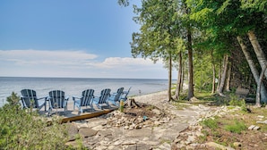 Ein Strandabschnitt mit Adirondack-Stühlen, einer Holzterrasse und einem Kiesweg zum Wasser.