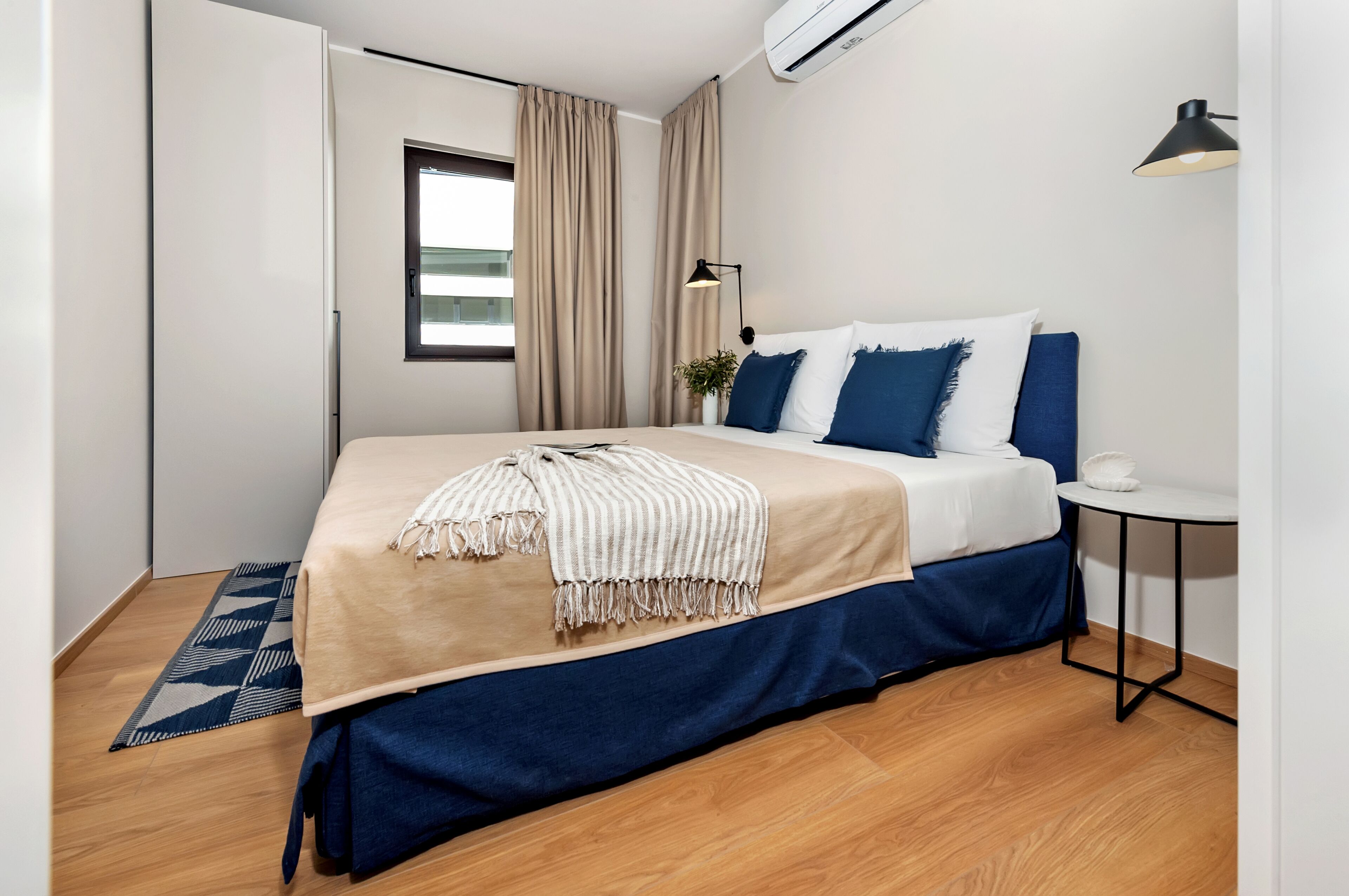 Un dormitorio moderno con cama, una mesita y una ventana.