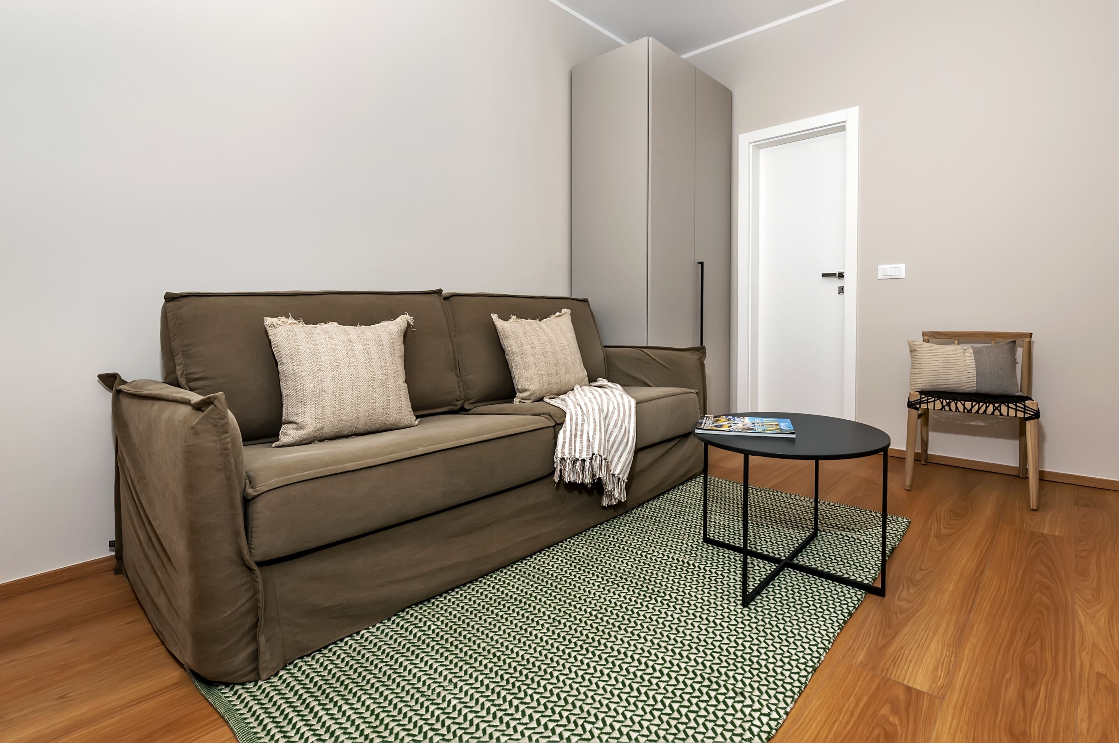 A modern living room with a brown sofa, two pillows, a small round table, and a chair.