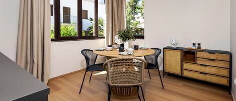 A modern dining area with a round table, four chairs, a buffet cabinet, and a potted plant.