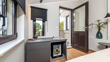 A compact room with a built-in mini-fridge, a desk with a computer, a bed, and a door leading to an outdoor area.