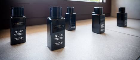 A set of black shower gel bottles labeled "NOIR" on a windowsill.