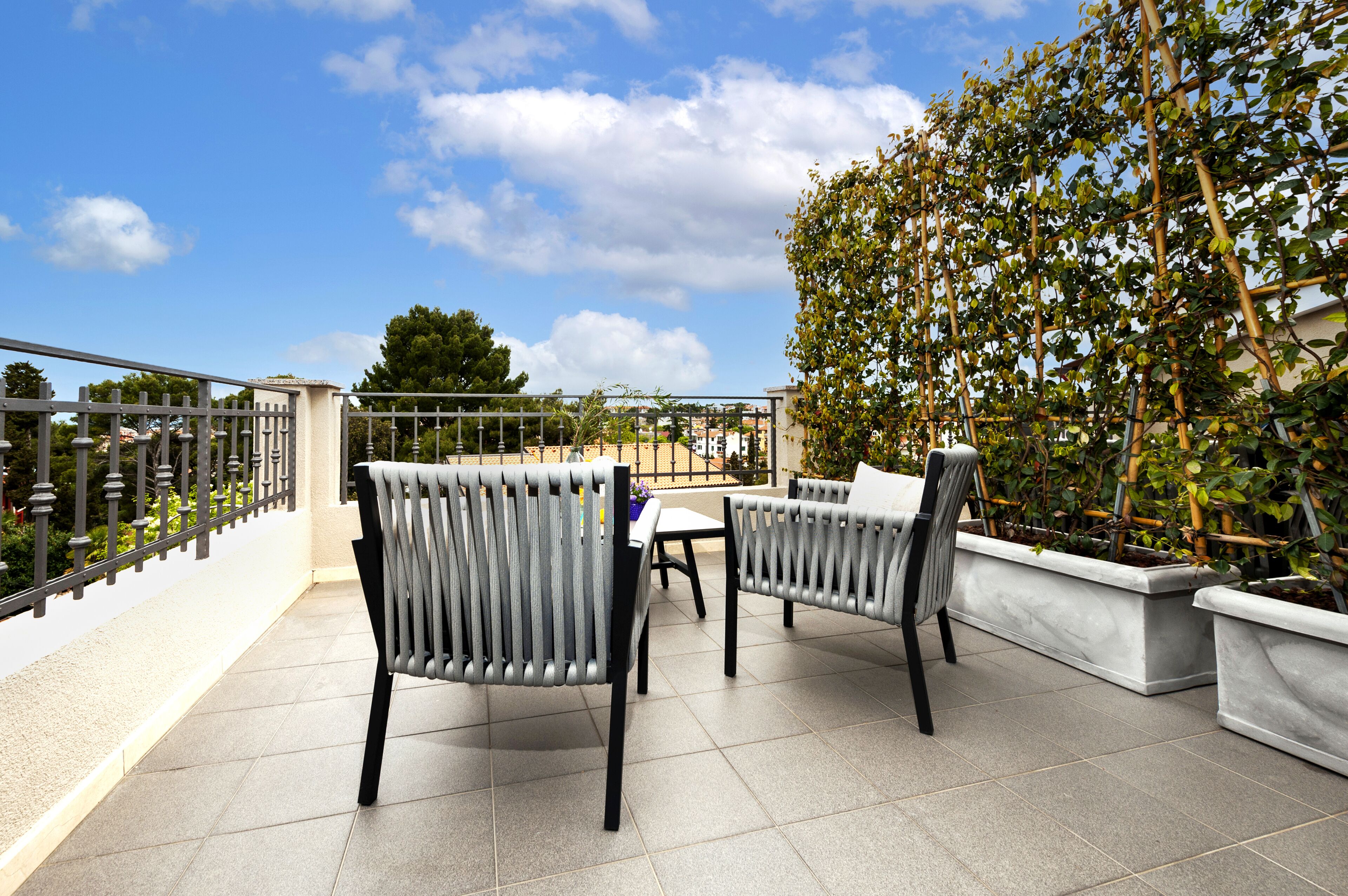 A terrace with two chairs and a table, surrounded by a metal railing and a hedge.