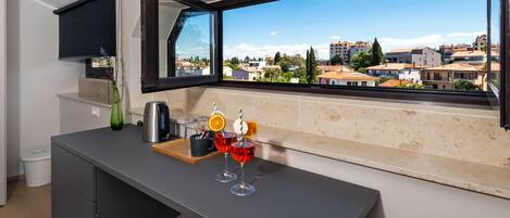 A modern kitchen with a large window, a coffee machine, and two glasses of red drink with orange slices.
