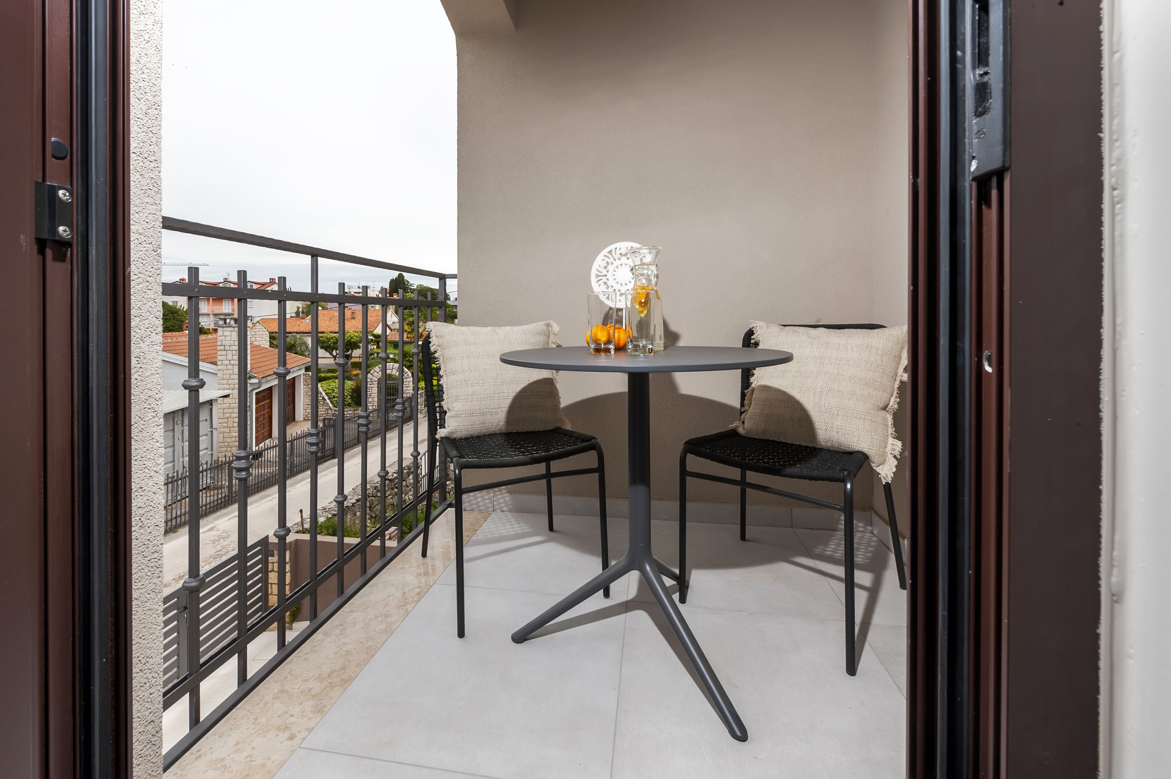 Un balcon avec une table ronde et deux chaises, un pichet décoratif en verre et un chemin de table blanc.