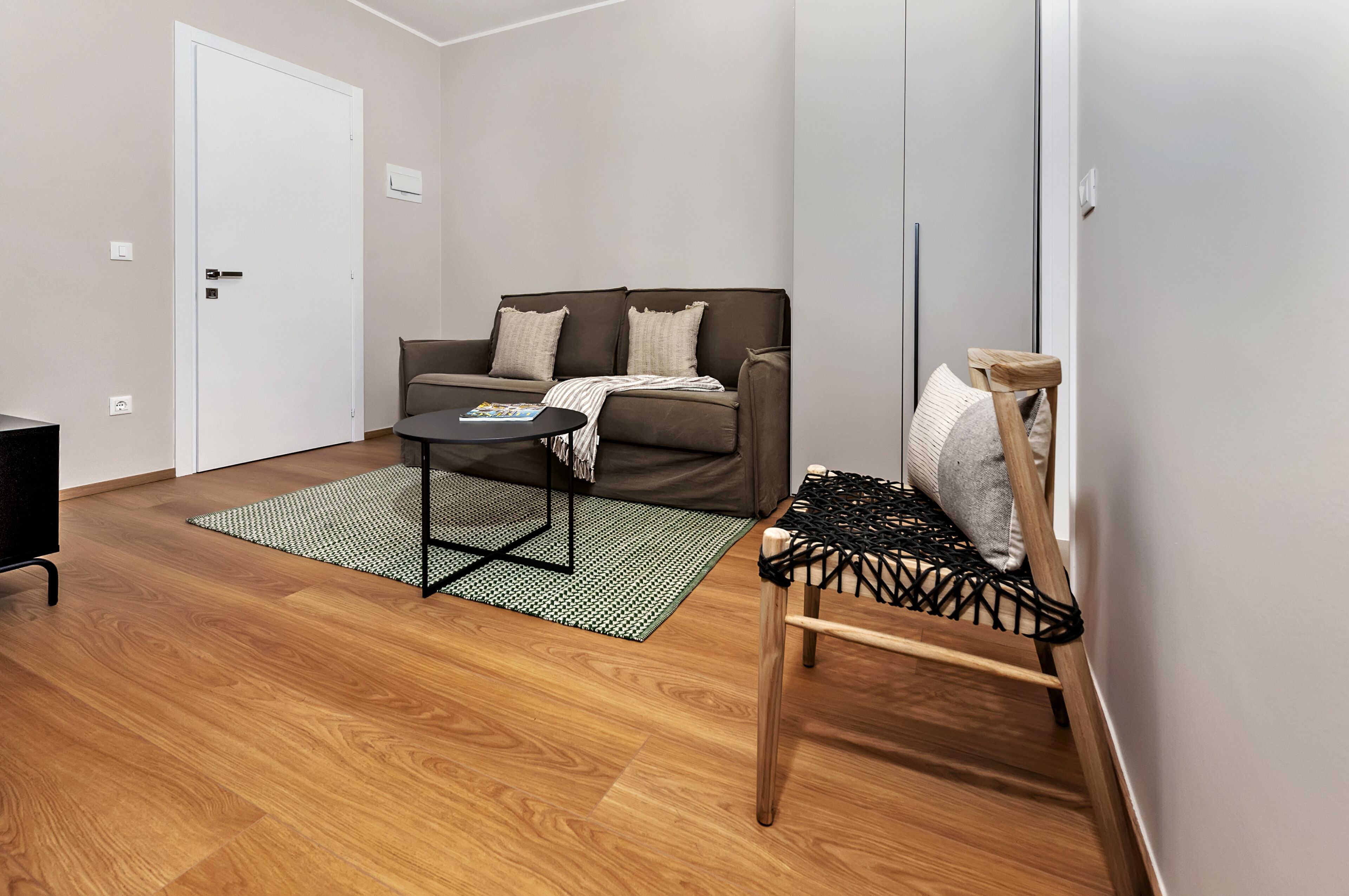 Una sala de estar moderna con un sofá marrón, una mesita redonda pequeña y una silla de madera con asiento de mimbre.