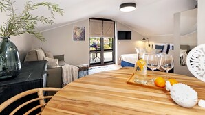 Una habitación moderna y luminosa con una mesa de comedor de madera, un florero con plantas verdes y vistas al balcón exterior.