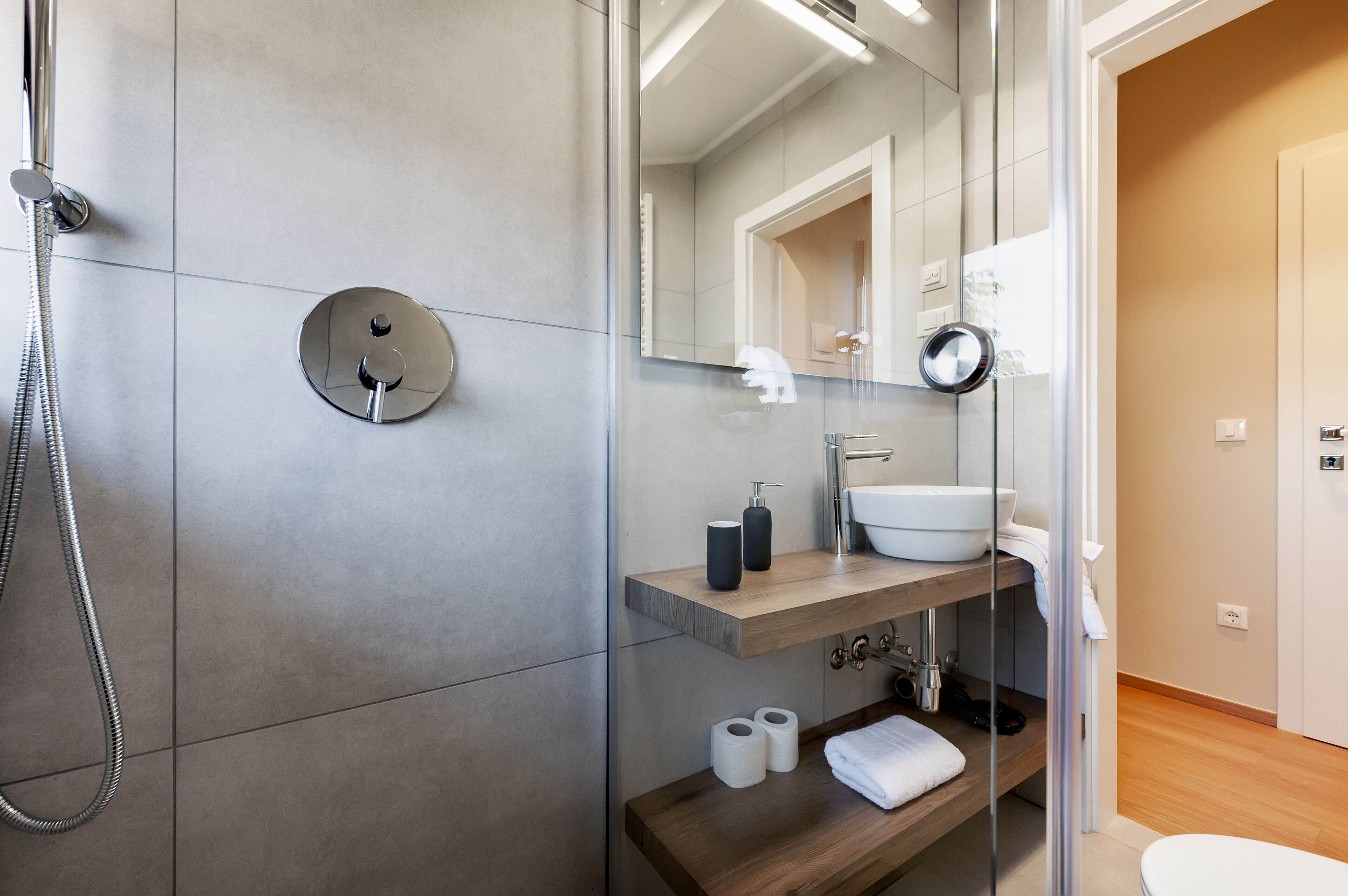 Een moderne badkamer met een douchecabine van glas, een houten wastafelmeubel met een wastafel en een spiegel erboven.