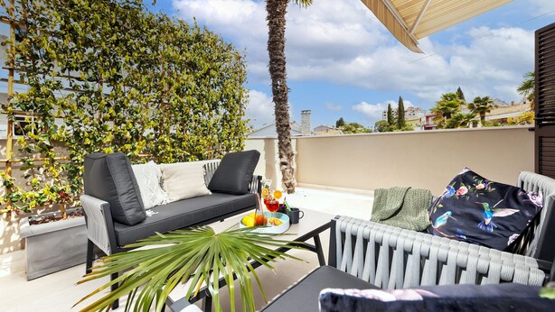Una terraza en la azotea con un sofá, sillas, una mesa y una palmera.