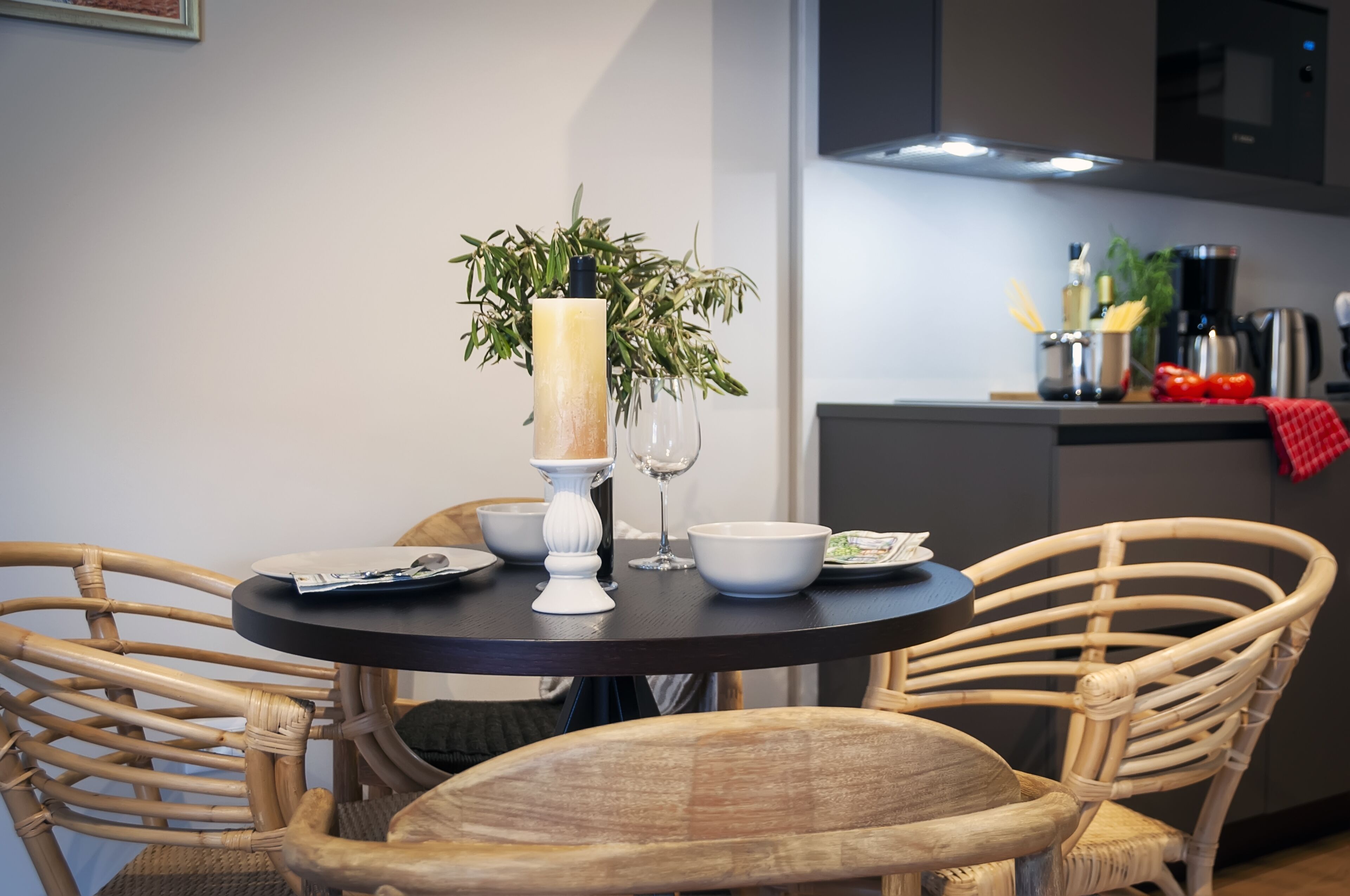 A dining area with a round table, wicker chairs, a vase with a candle, and a potted plant.