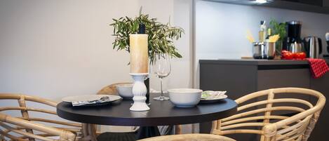 A dining area with a round table, wicker chairs, a vase with a candle, and a potted plant.