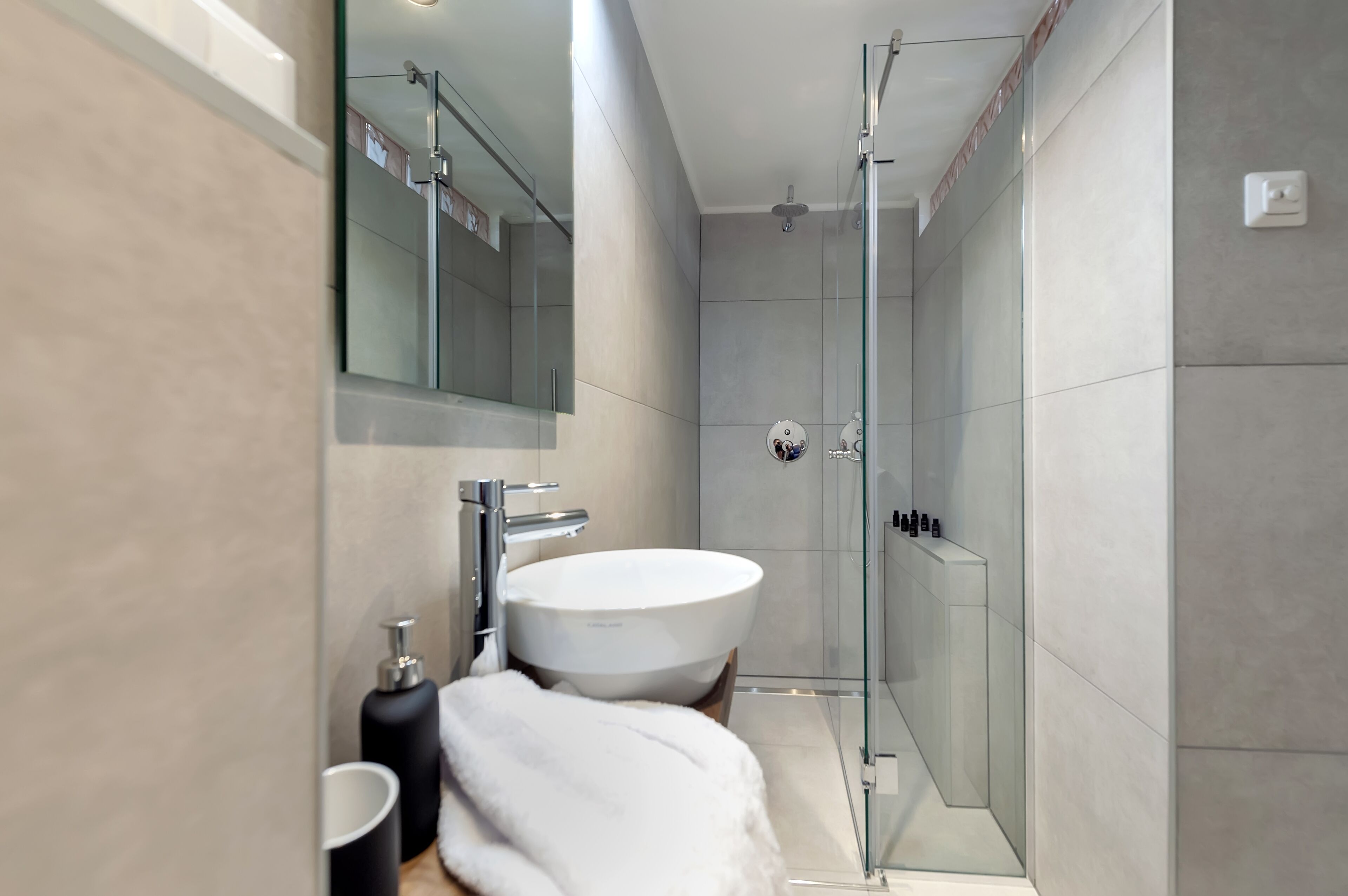 Un baño moderno con un lavamanos grande de color blanco, una cabina de ducha con paredes de vidrio y un espejo sobre el lavamanos.