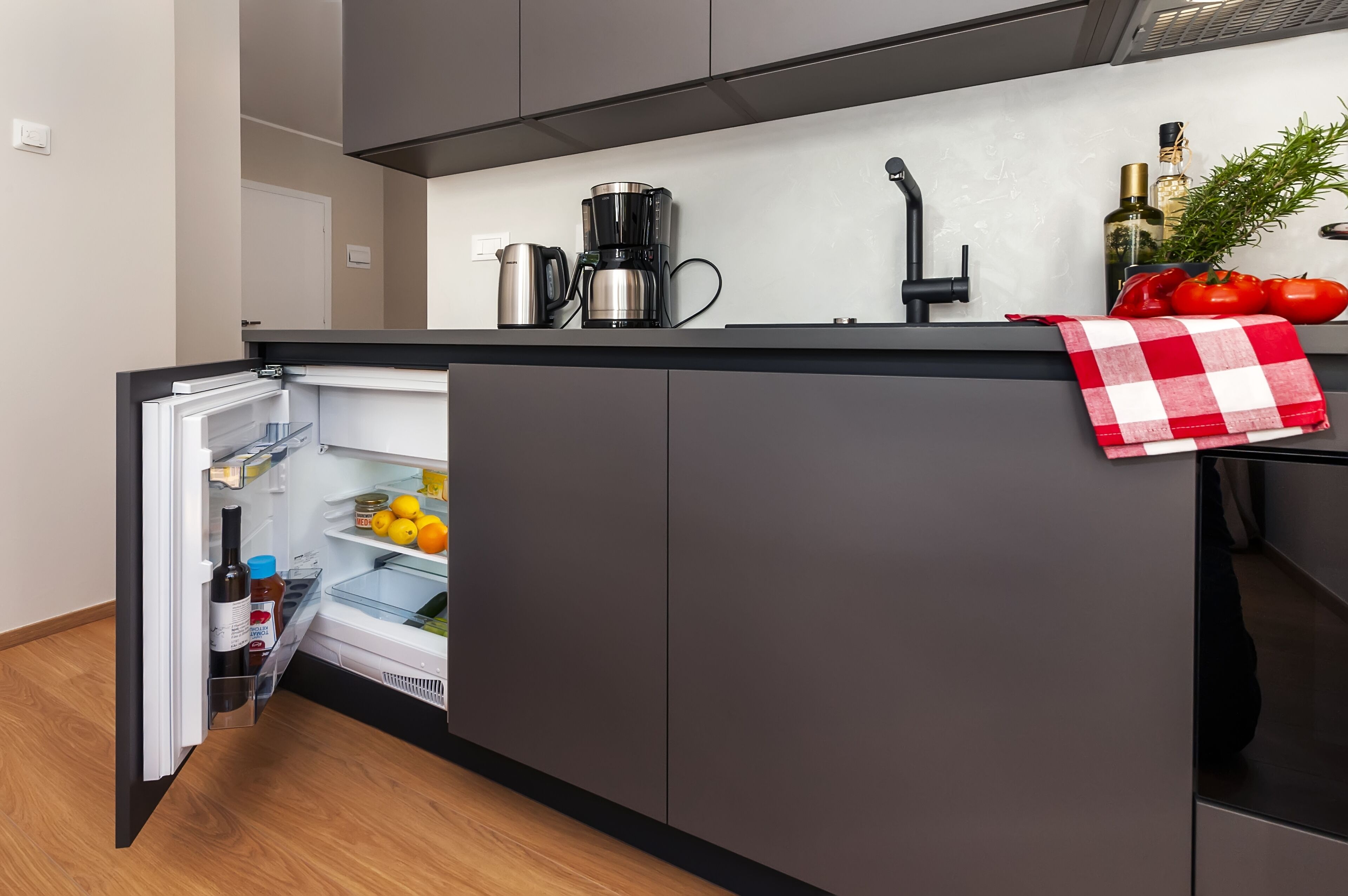A modern kitchen with a built-in refrigerator, a coffee maker, and a countertop with a red and white checkered towel.
