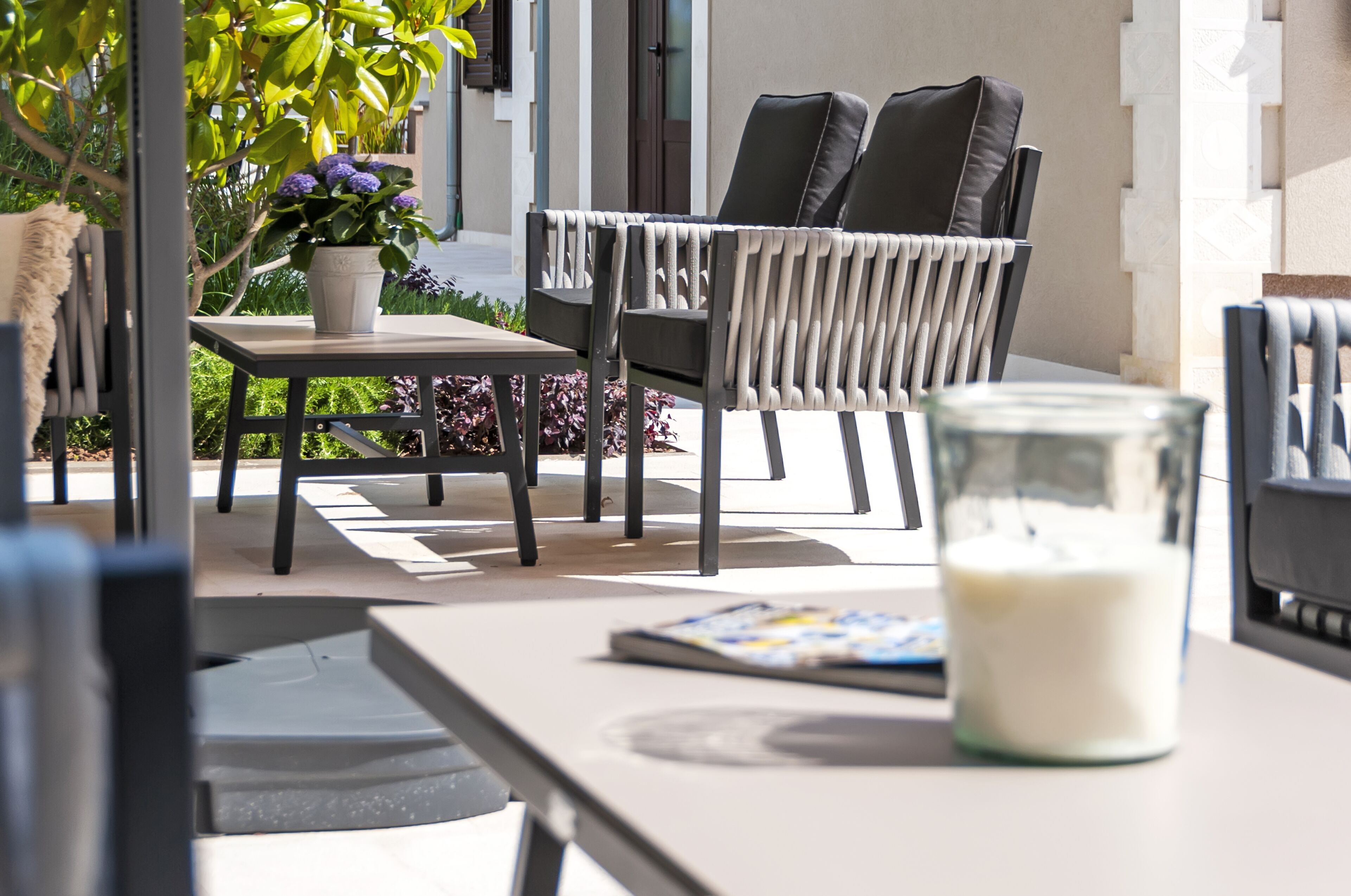 An outdoor seating area with a table, chairs, a potted plant, and a glass of milk.
