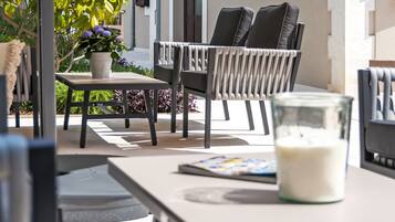 An outdoor seating area with a table, chairs, a potted plant, and a glass of milk.
