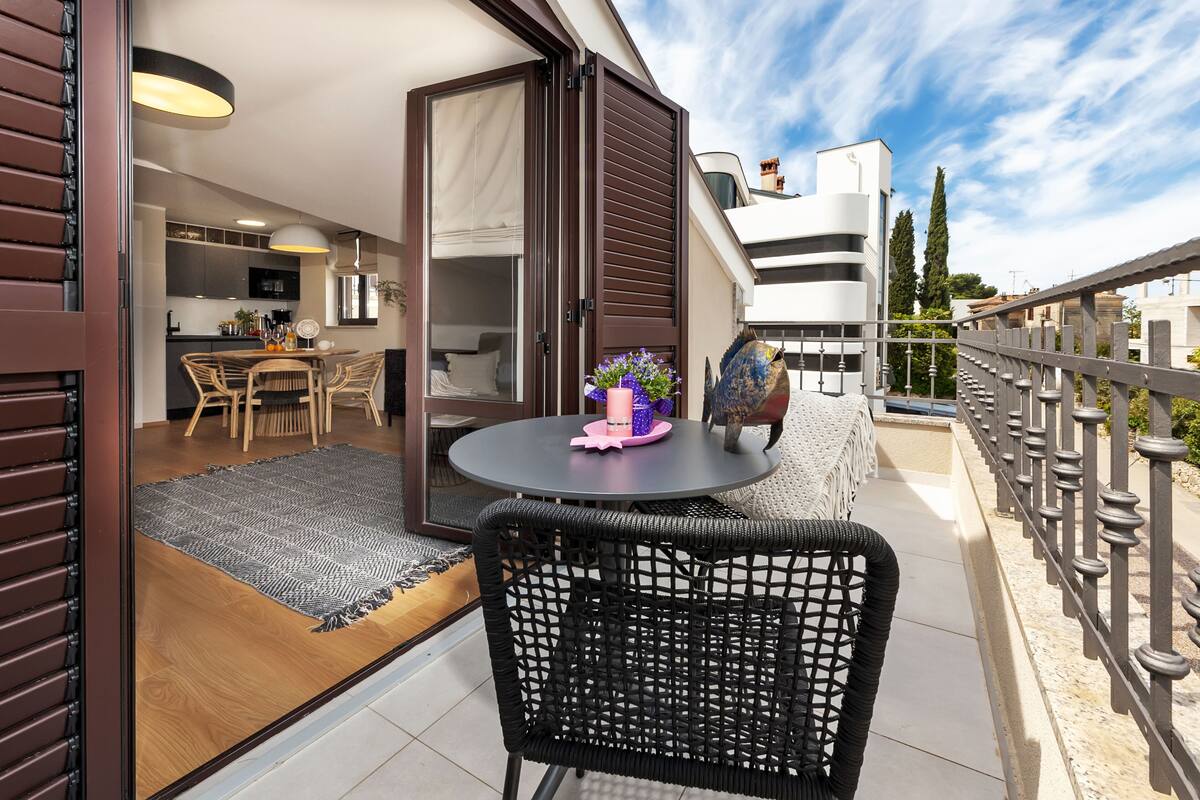 A balcony with a round table, wicker chairs, and a potted plant.