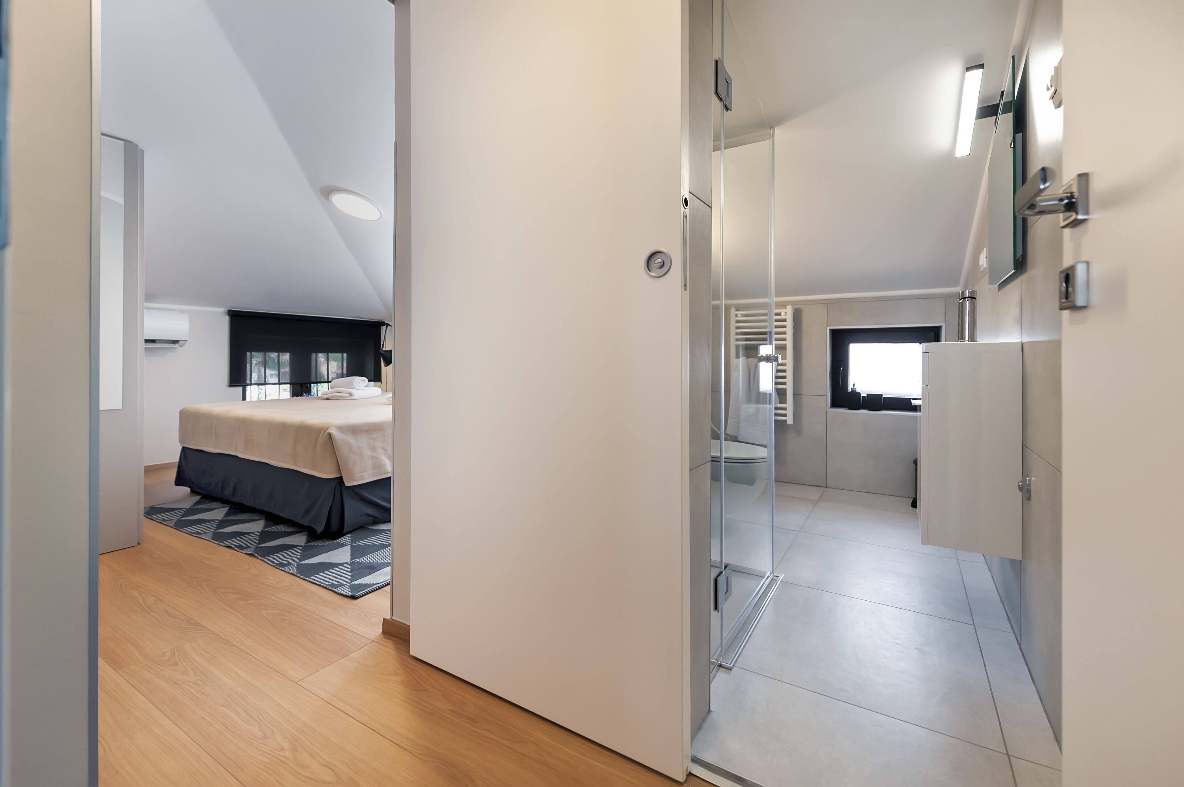 Una habitación de hotel moderna con cama, cabina de ducha de vidrio y kitchenette.