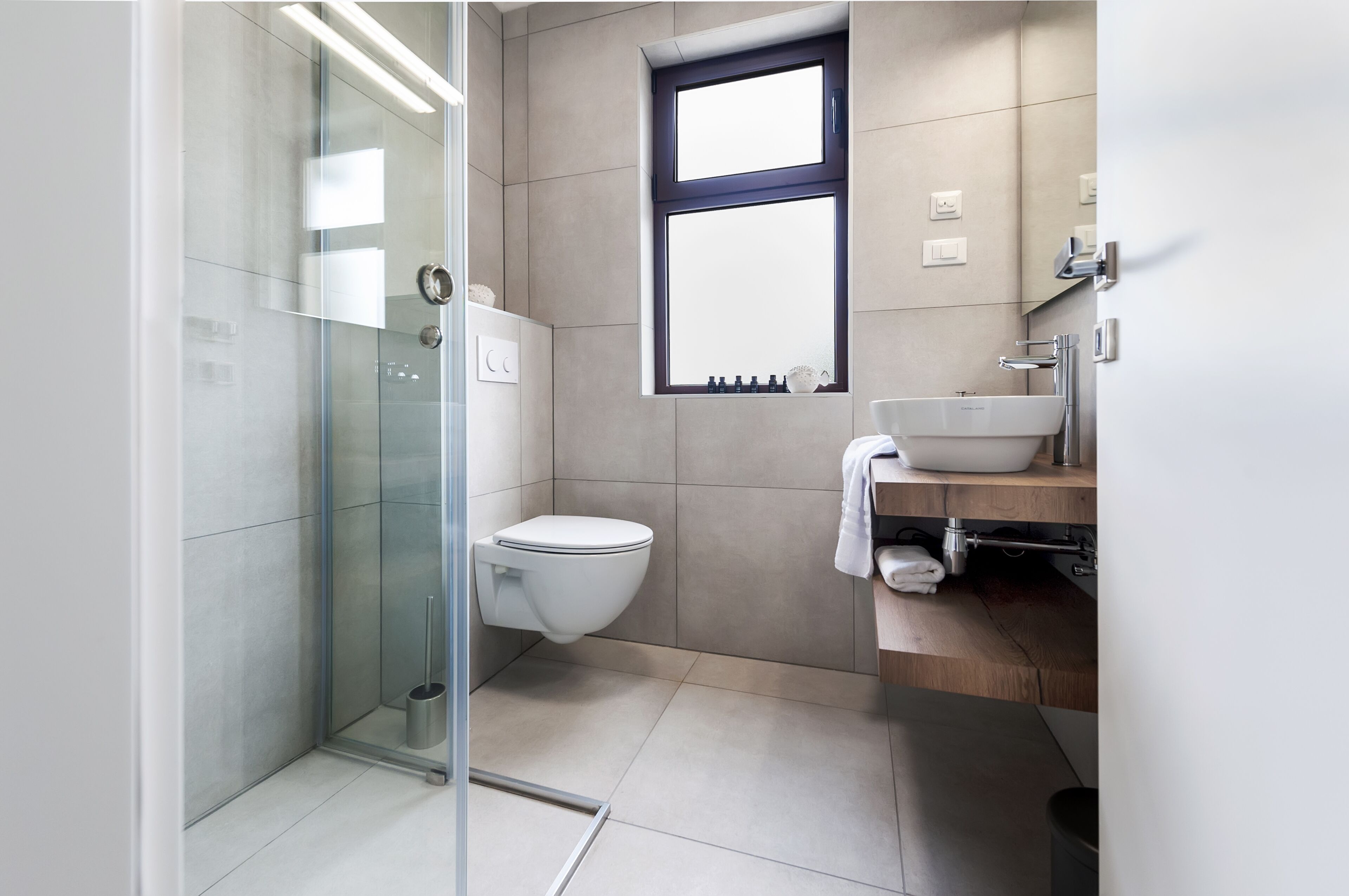 A modern bathroom with a glass shower enclosure, a white toilet, and a wooden vanity with a sink.