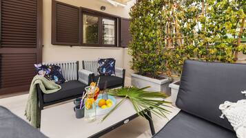 Un rincón exterior acogedor con un sofá, una mesa con bebidas y frutas, y una planta en maceta.
