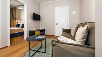 A compact hotel room with a bed, a sofa, a small table, a TV, and a door.