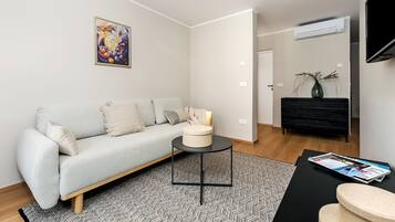 Een moderne woonkamer met een lichtgrijze bank, een ronde zwarte salontafel en een zwarte tv-meubel.