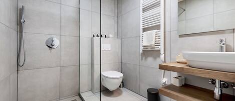 Un baño moderno con ducha de vidrio, inodoro, lavamanos con encimera de madera y espejo sobre el lavamanos.