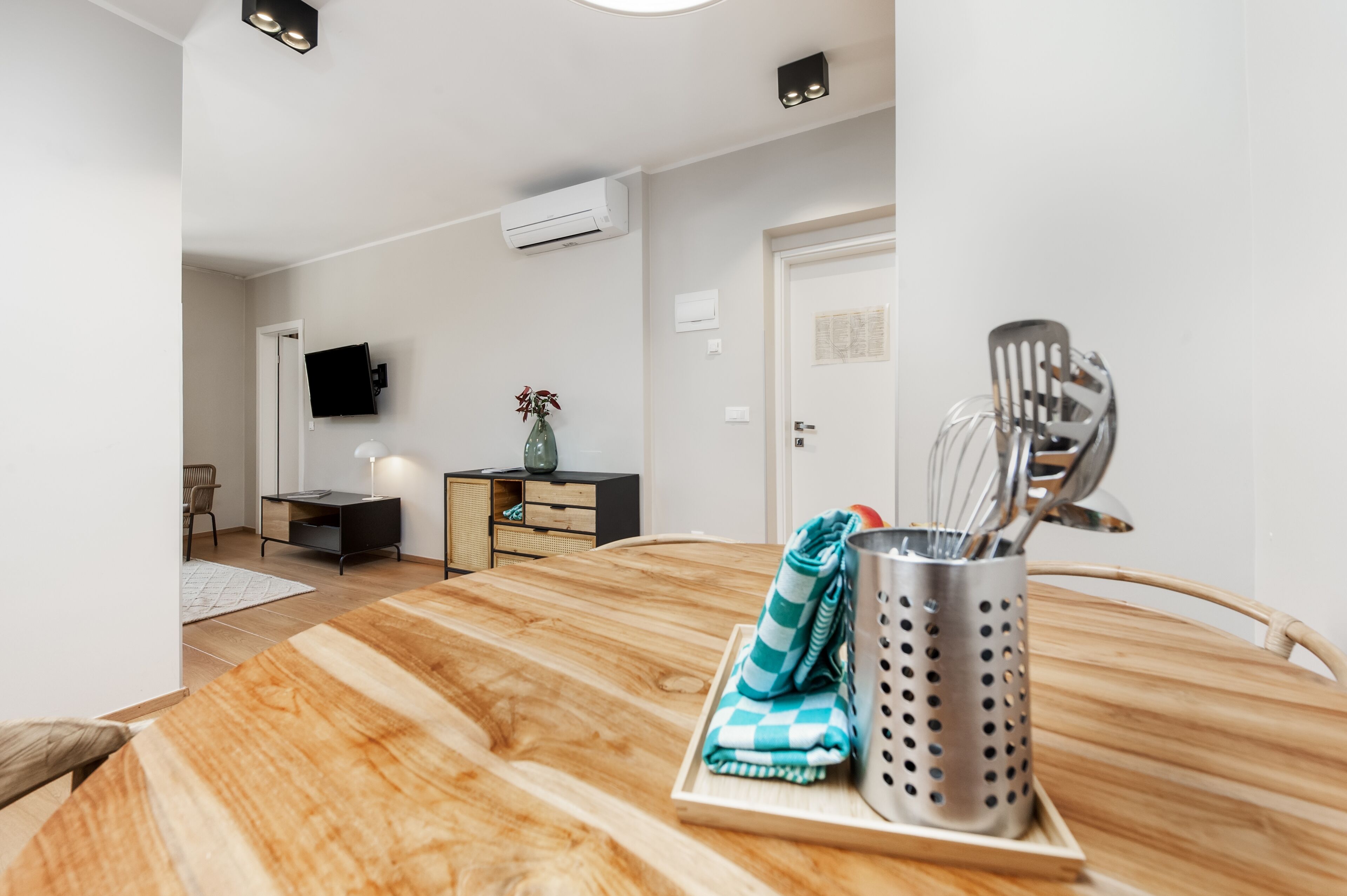 Uma cozinha moderna com uma mesa de madeira, um suporte de utensílios em aço inoxidável e uma televisão de tela plana fixada na parede.