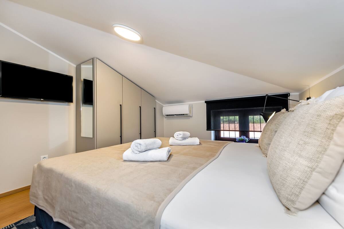 A bedroom with a bed, a TV mounted on the wall, and a window with a view.