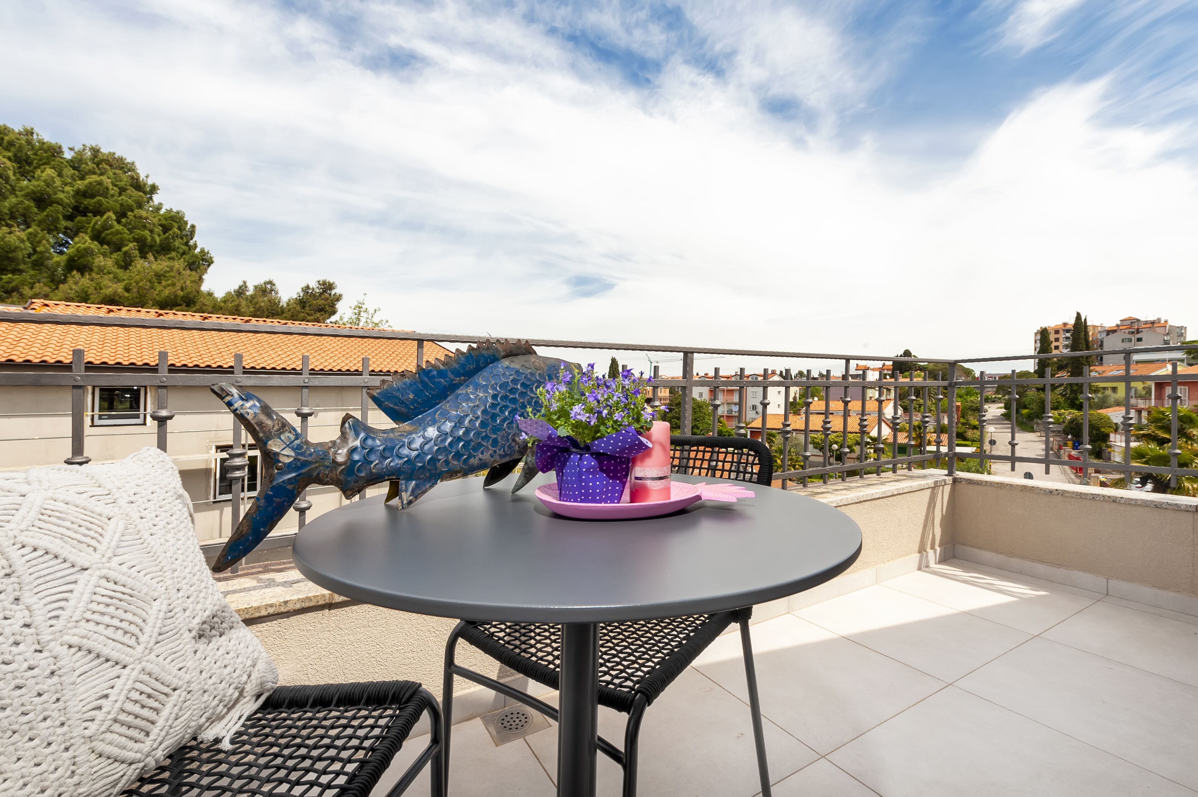 A round table with a chair, a decorative blue dragon sculpture, and a purple flower arrangement on the balcony.