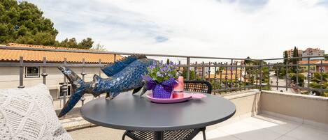 A round table with a chair, a decorative blue dragon sculpture, and a purple flower arrangement on the balcony.