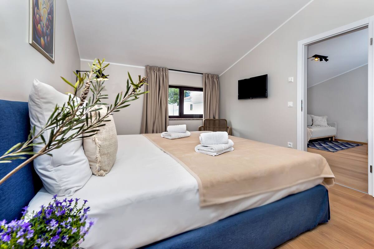 A modern hotel room with a large bed, a TV, and a window with curtains.