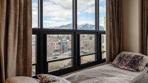 Una camera da letto con un'ampia finestra, un letto e vista sulla città e sulle montagne.