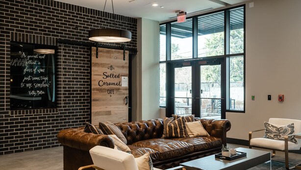 Un'area lounge moderna con un divano in pelle, un tavolino in vetro e una poltrona bianca. Un cartello appeso al muro recita: “Salted Caramel Cafe.”