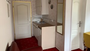 Eine kompakte Küche mit Spüle, kleinem Kühlschrank und Spiegel. Eine Tür mit goldenem Rahmen und ein Teppichboden in Rot.