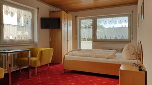Ein Zimmer mit einem Bett, einem Schreibtisch, einem Sessel, einem Fernseher und großen Fenstern.