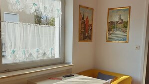 Una habitación con una mesa blanca, sillas amarillas, un radiador y una alfombra roja.