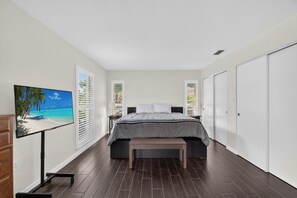 Une chambre à coucher comprenant un lit, une table de chevet, un banc, un téléviseur et une fenêtre avec des stores.