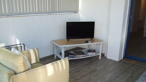 Una habitación con un sofá, una mesita con televisión y una estantería.