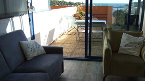 Un balcón con sofá, sillón, una mesa y vista al mar.